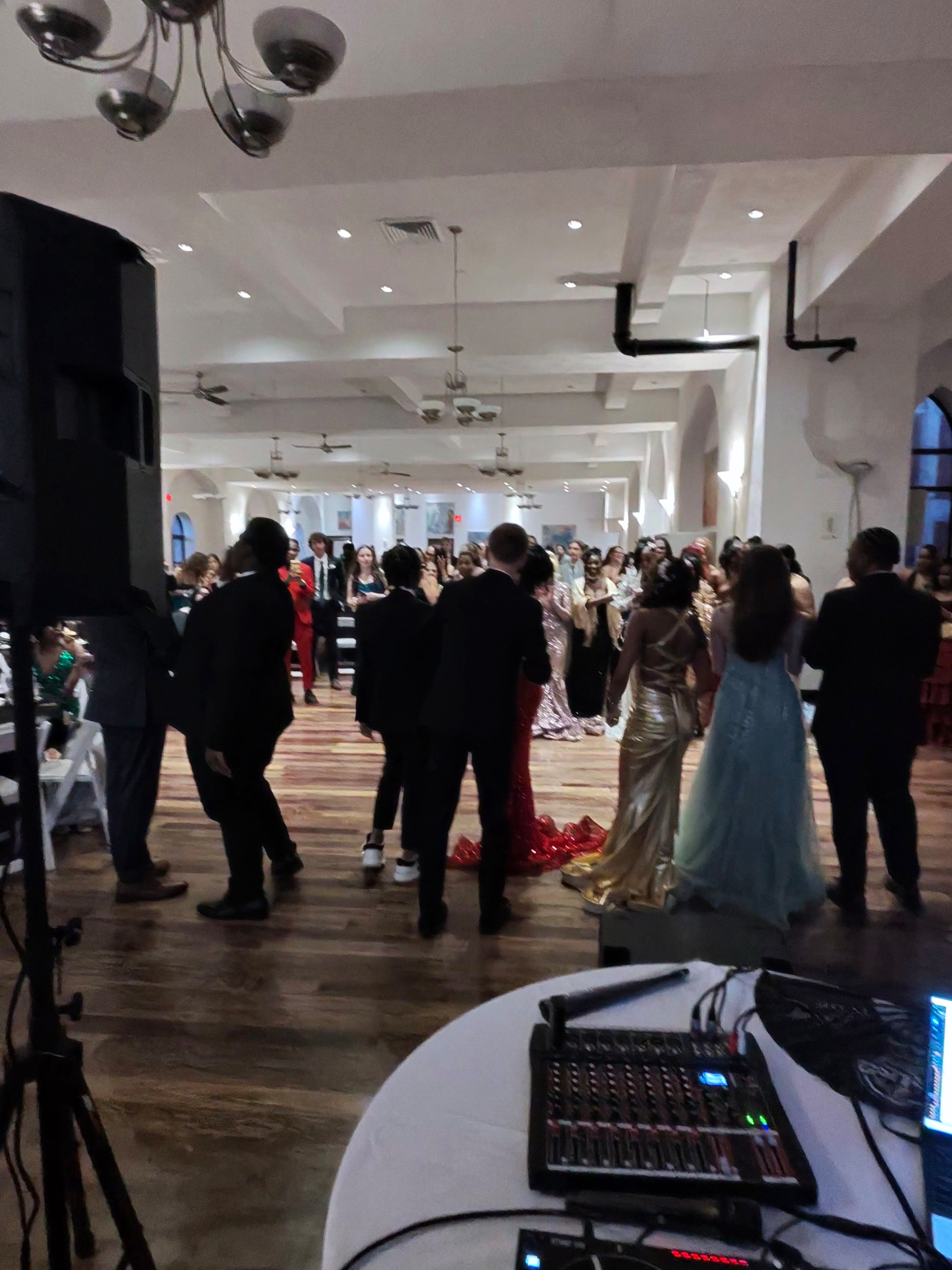 Students in formalwear gathered on the dance floor at a St. Louis area prom with DJ Sir Uso's sound and lighting setup in the foreground